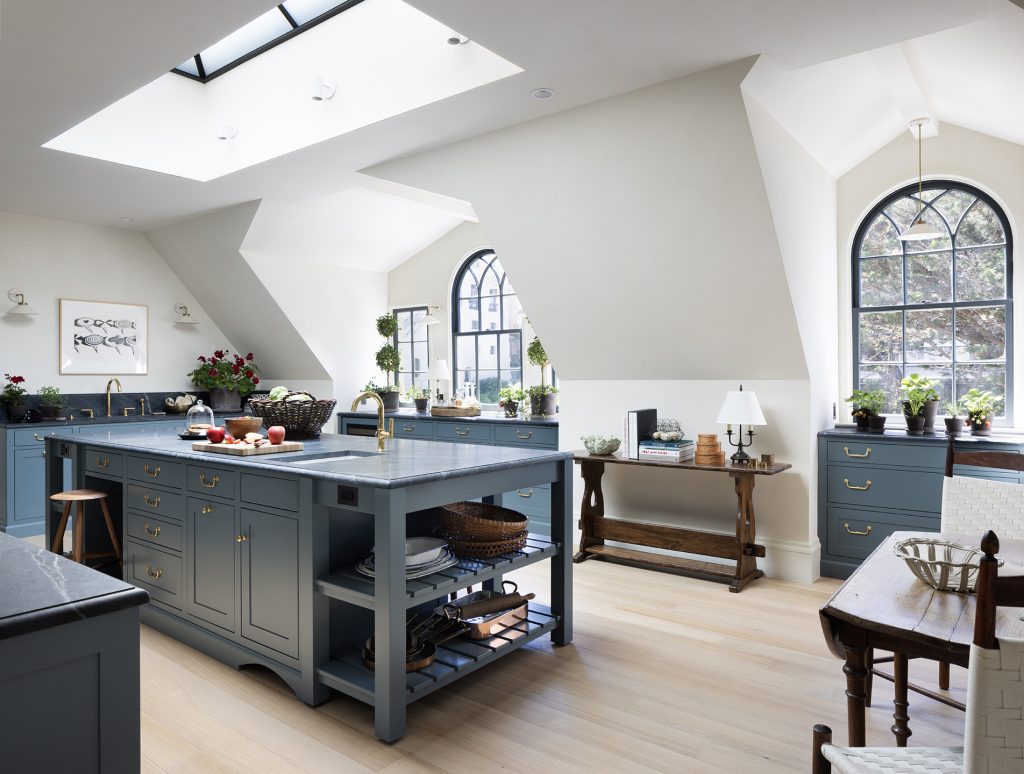 Bright kitchen with blue cabinets, a large island, skylight, arched windows, plants, and wood accents. Light wood floors and white walls create an airy, inviting atmosphere with plenty of natural light.